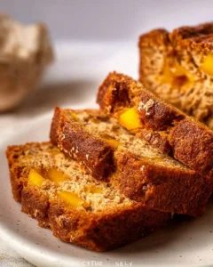 Loaf of easy mango bread on a wooden table, garnished with fresh mango slices